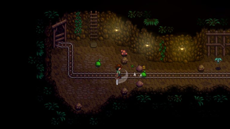 A Stardew Valley farmer fighting slimes beside a mine rail in a dark cavern