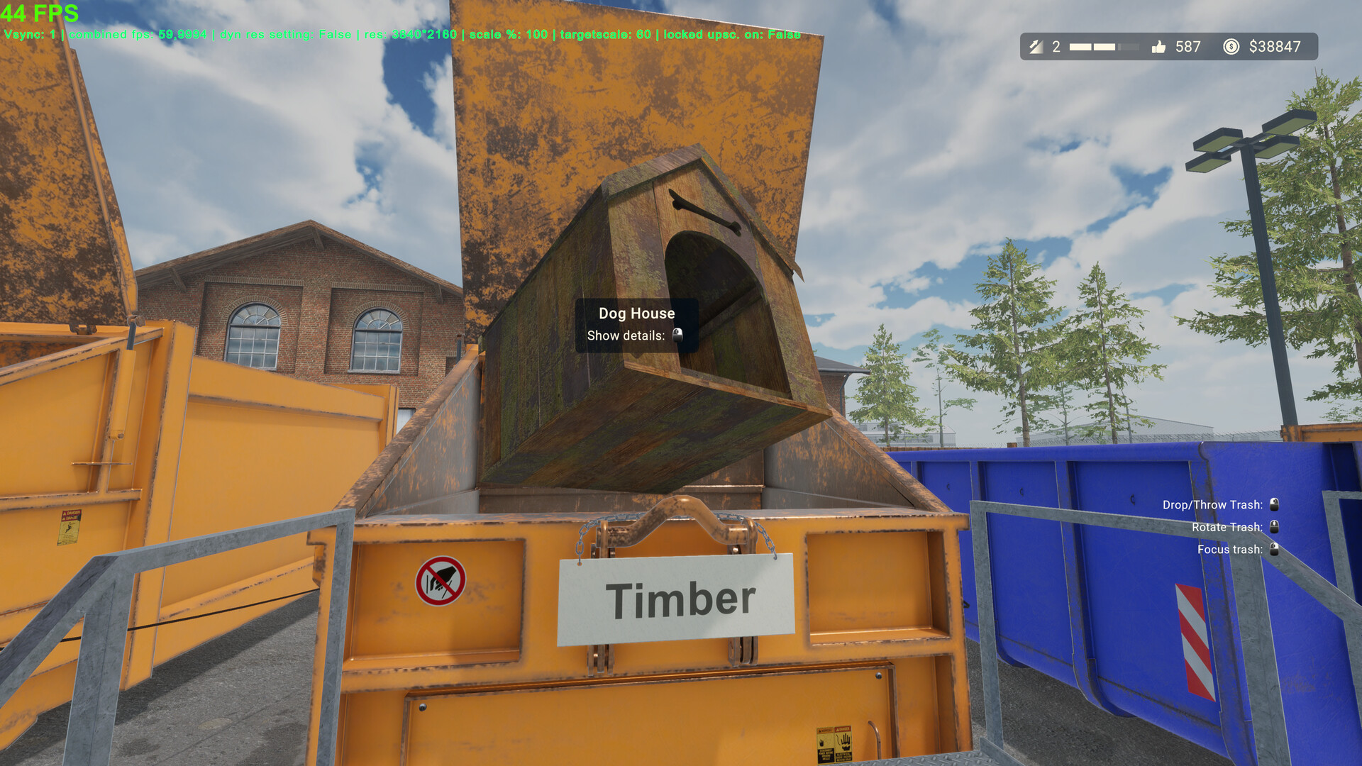 A held wooden dog house positioned over the mouth of a compactor labeled Timber
